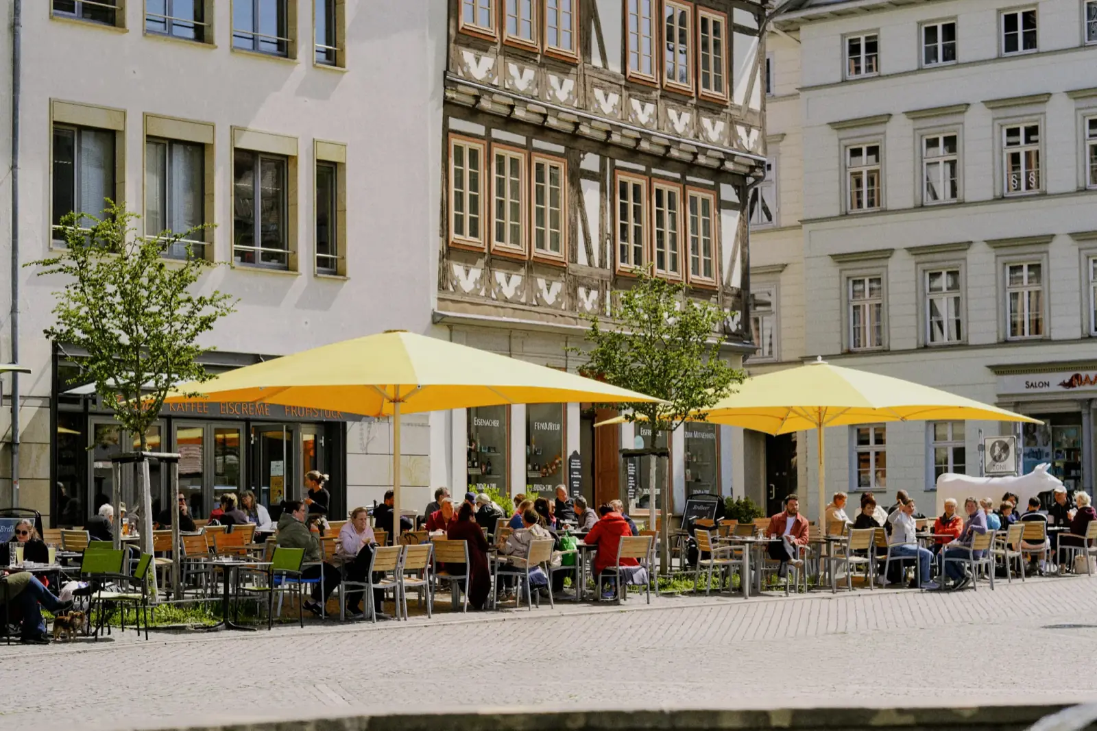 Café Toccata Terrasse am Eisenacher Marktplatz mit gelb-orangen Sonnenschirmen und Gästen